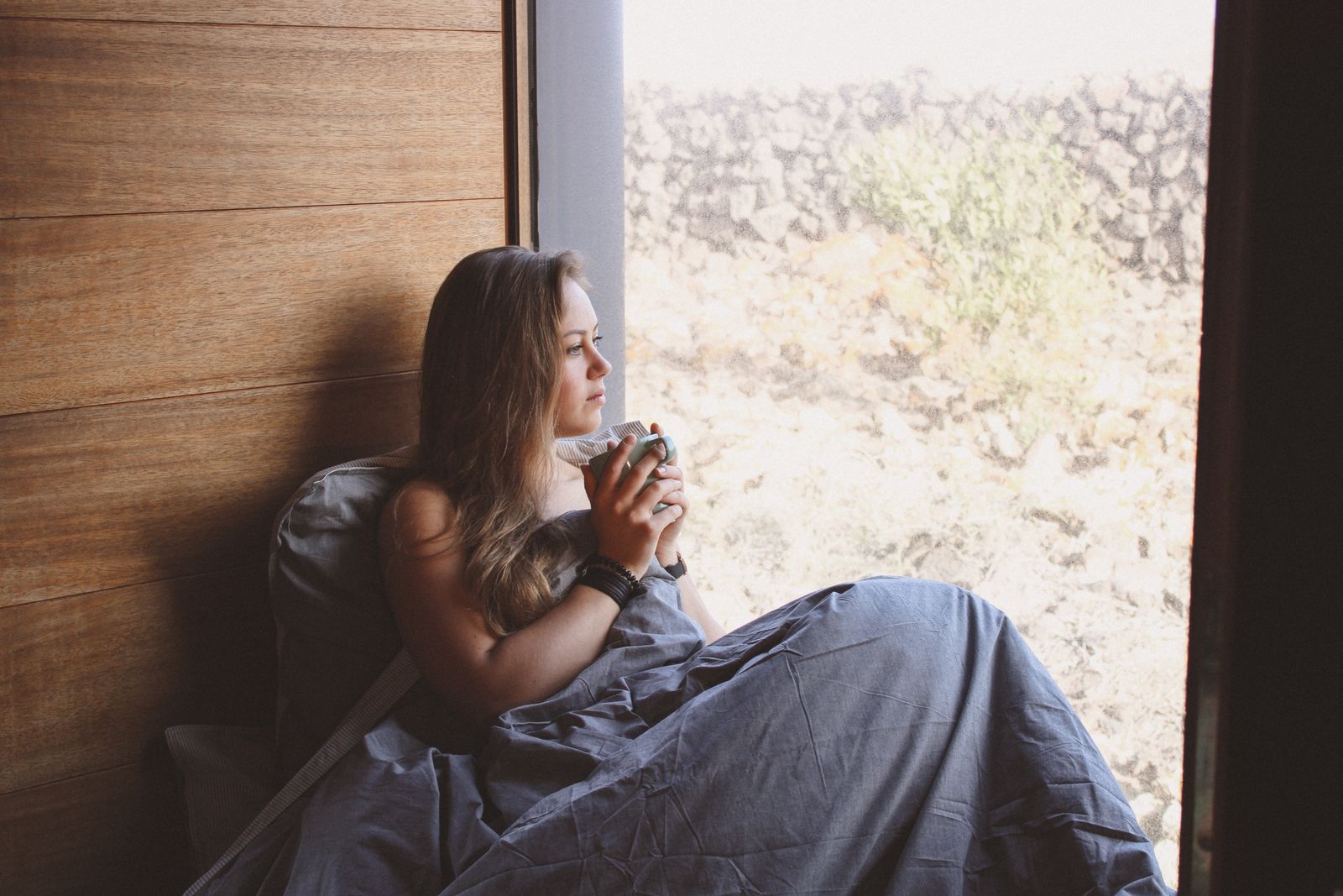 A person holding a cup beside a window