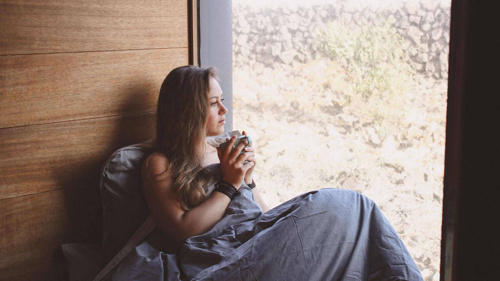 A person holding a cup beside a window