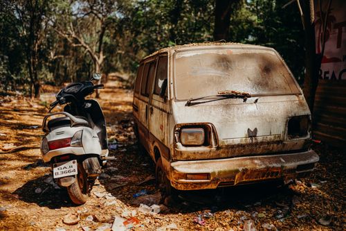 Free Abandoned rusty van and scooter under trees on a sunny day, highlighting decay and nature. Stock Photo