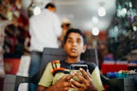 一个小男孩在室内专注地看着他的智能手机，背景是模糊的