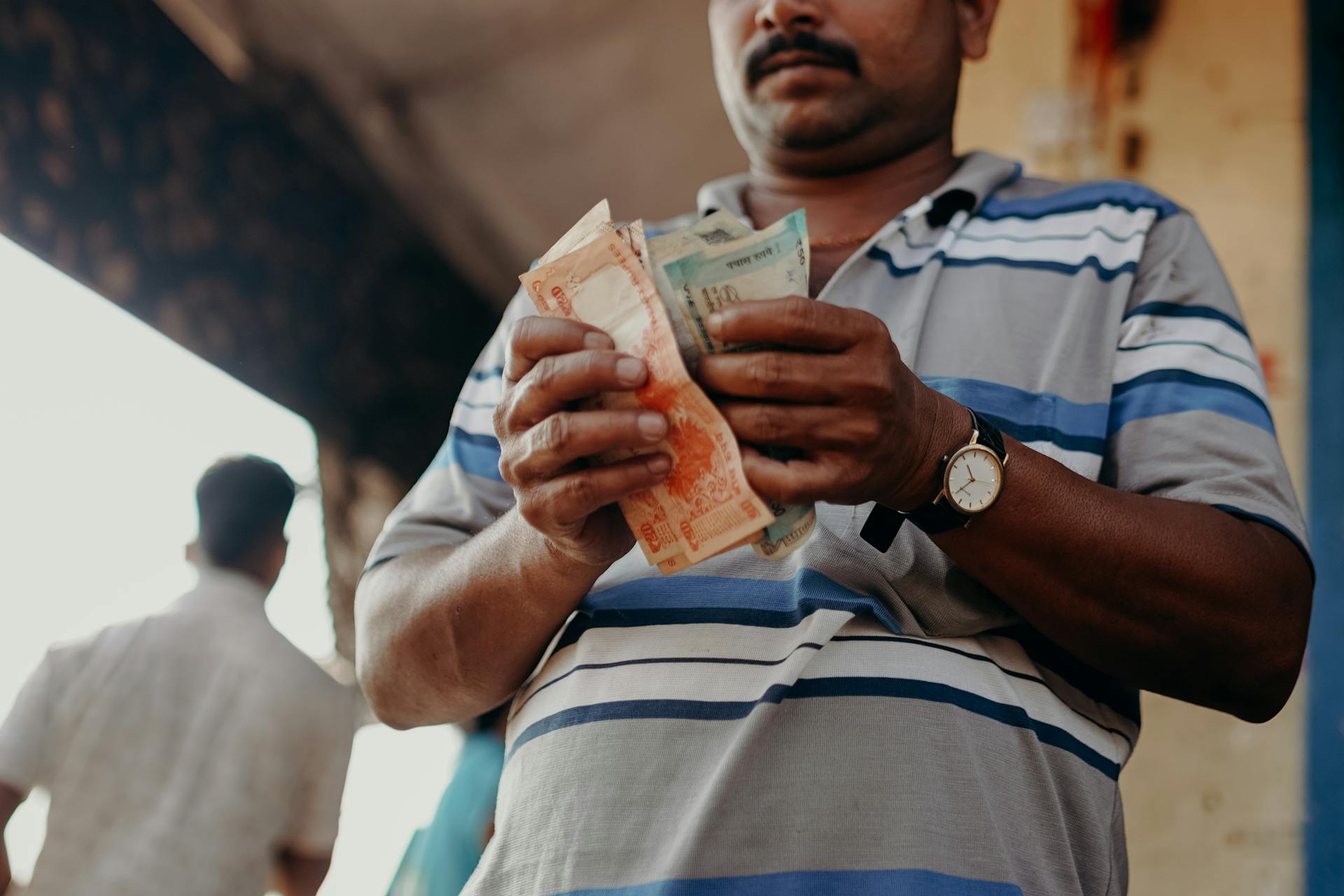 Man in Blue and White Stripe Polo Shirt Holding Banknote