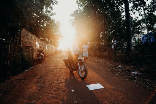 在印度一条阳光明媚的乡村道路上，一名男子骑着摩托车，周围都是绿色植物