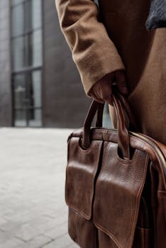 A person holding a brown leather bag, showcasing fashion and style in a city environment.
