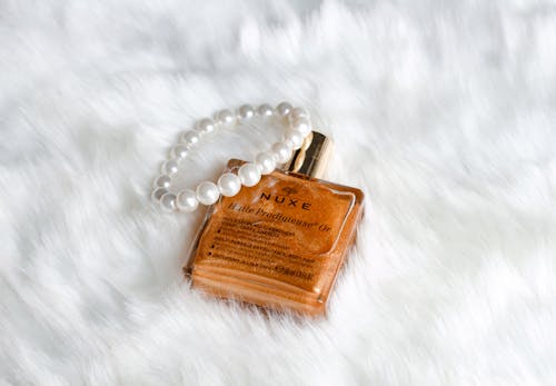 From above golden face oil in refined bottle placed with pearl bracelet on white cozy plaid