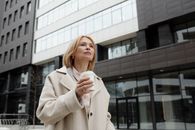 一位穿着米色外套的优雅女人，在现代建筑外拿着咖啡杯