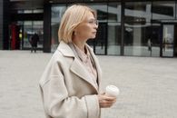 一位穿着米色外套的女人，自信地拿着咖啡站在城市街头