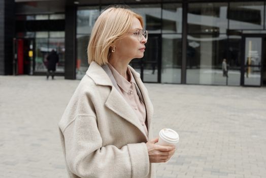 一位穿着米色外套的女人，自信地拿着咖啡站在城市街头