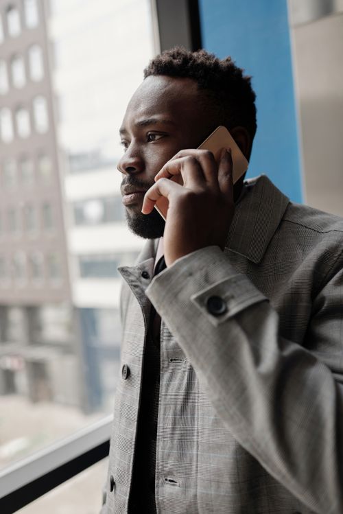Free Professional man in gray coat having a serious phone conversation while looking out the window. Stock Photo