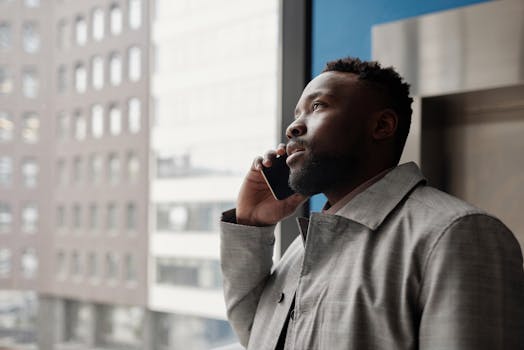 Business professional talks on phone near city window, modern urban background.