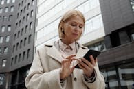 一位穿着外套的女人在现代建筑前专注地使用着智能手机