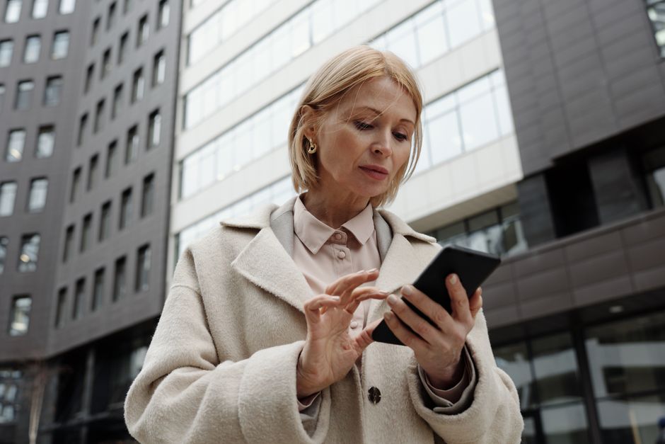 Woman in coat using smartphone in front of modern building. Professional and focused expression.