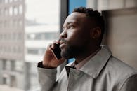 一名男子表情严肃地站在窗前，用智能手机打电话