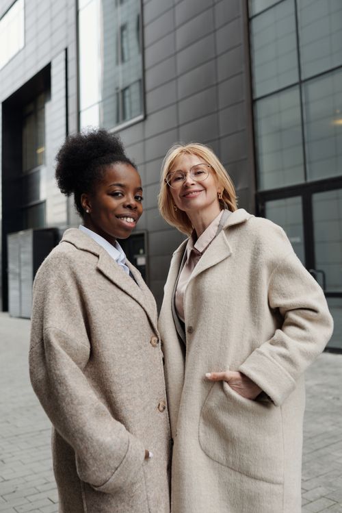 Free Two professional businesswomen smiling in stylish coats, captured outdoors in an urban setting. Stock Photo