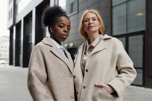 Free Two diverse businesswomen in stylish coats posing confidently on a city street. Stock Photo