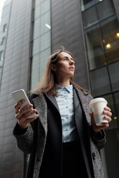城市里，一位职业女性手持智能手机和咖啡杯，抬头仰望