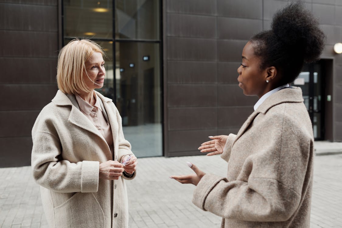 Free Two businesswomen in coats converse outside a modern office building. Stock Photo