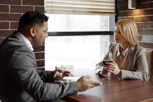 Free Two business professionals discussing ideas over a glass of wine in a modern café setting. Stock Photo
