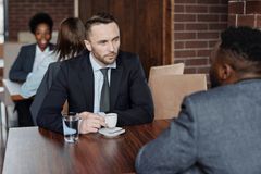 Two businessmen in suits discussing over coffee during a meeting in a café.