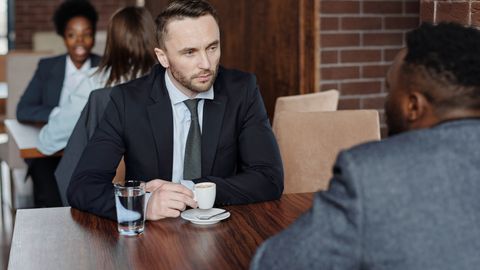 Two businessmen in suits discussing over coffee during a meeting in a café.