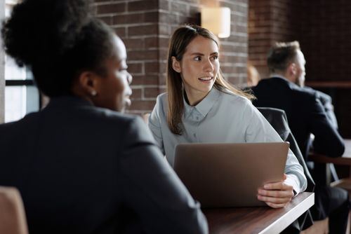 Free Business professionals engaged in conversation at a modern café with laptops. Stock Photo