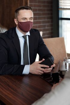 商务会议期间，一名西装革履、戴着口罩的男子坐在桌旁