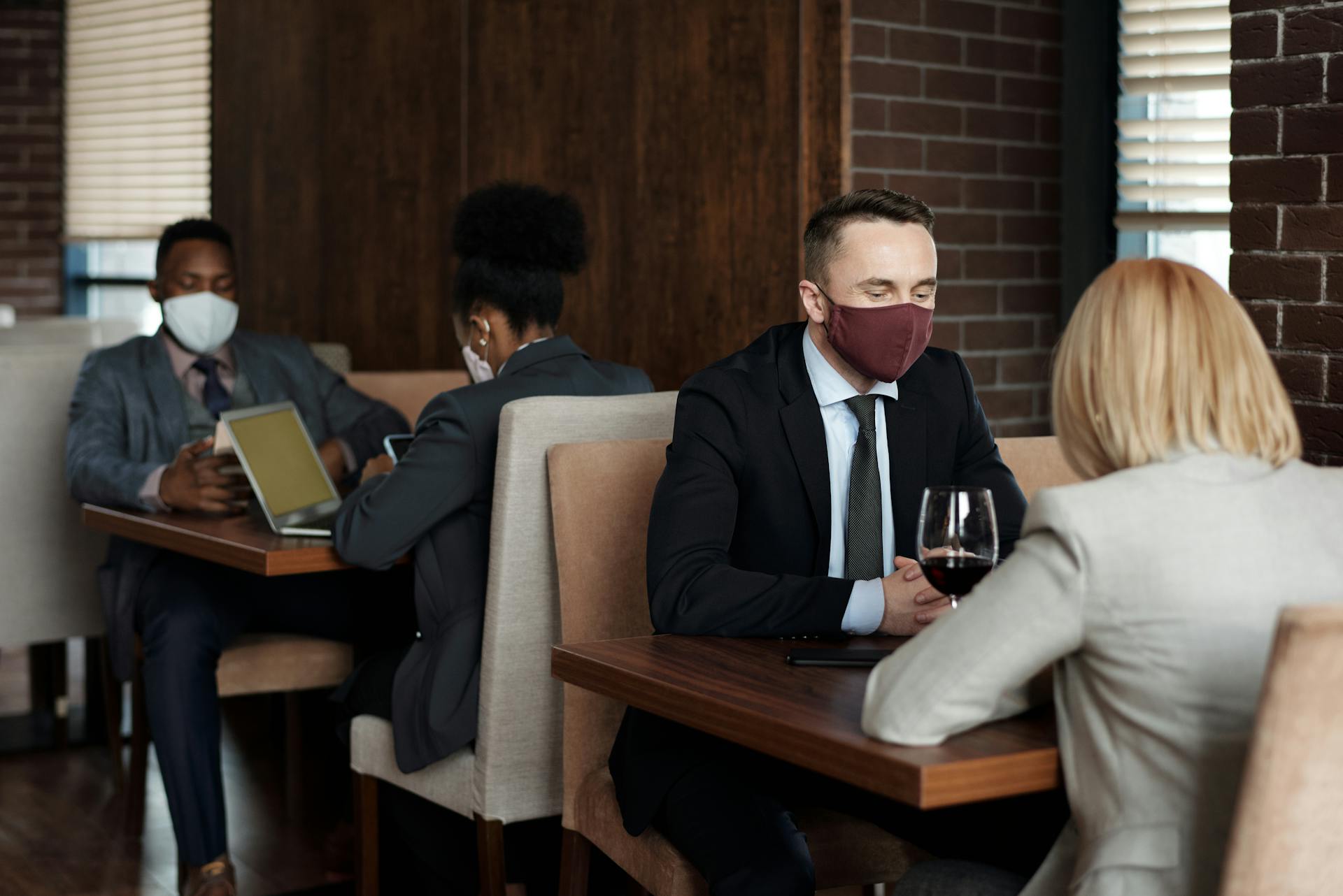 Office workers wearing masks in a café meeting, ensuring pandemic safety with social distancing.