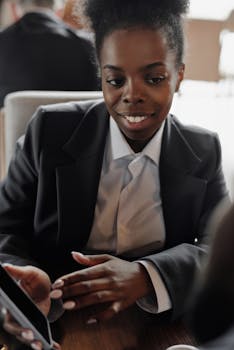 Elegant businesswoman in a blazer engaged with her smartphone indoors, smiling and professional.