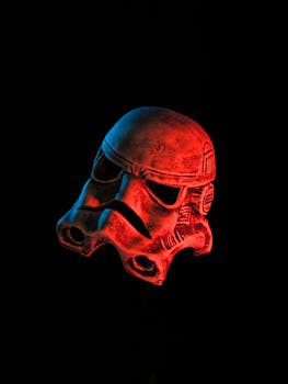 Close-up of a weathered stormtrooper helmet with red and blue lighting on a dark background.