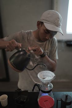 Young man skillfully brewing coffee with a pour-over method indoors, showcasing precision and focus.