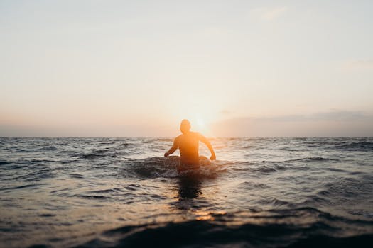 Silhouette of a man entering the ocean during a peaceful beach sunset scenic view.