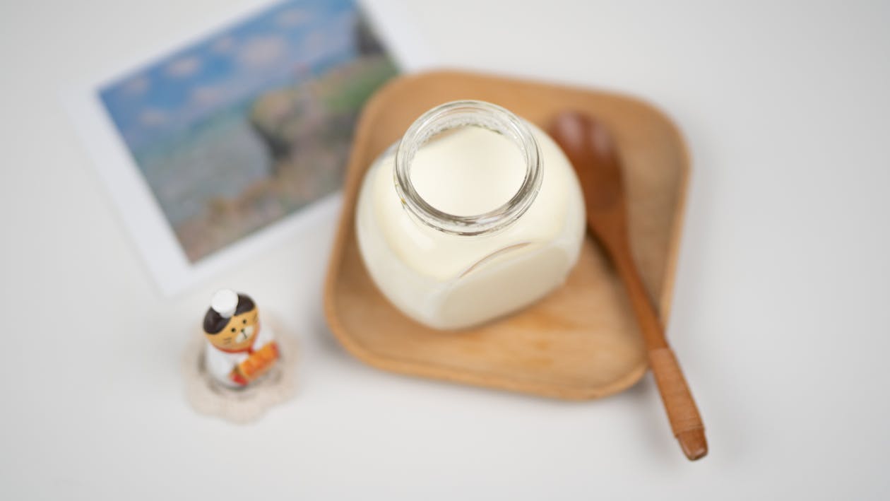  above arrangement of fresh milk yogurt in glass jar placed on wooden saucer near funny cat figurine 
