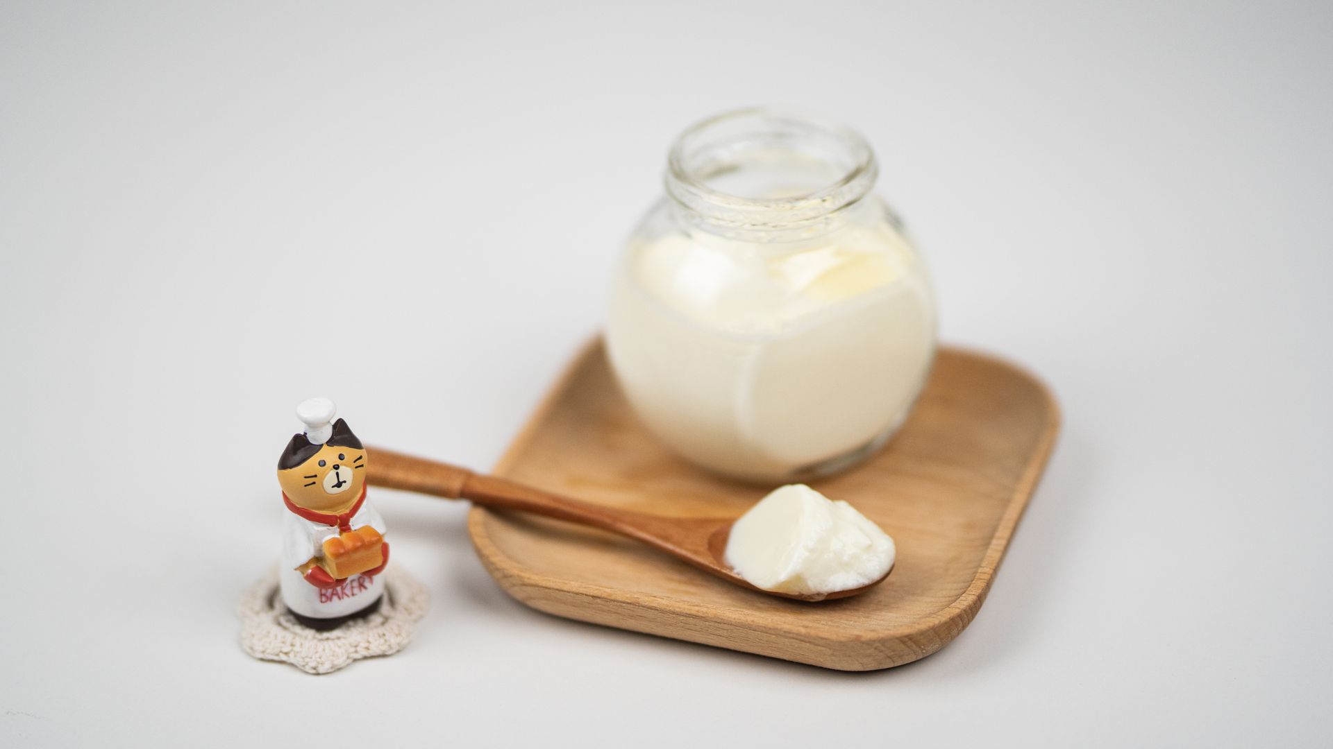Jar with delicious plain yogurt and wooden spoon on saucer