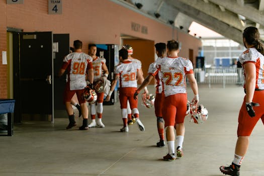 Group of football players in uniforms walking into locker room after game.
