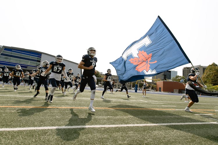 People In Black Uniform Holding Blue Flag Running On Football Field