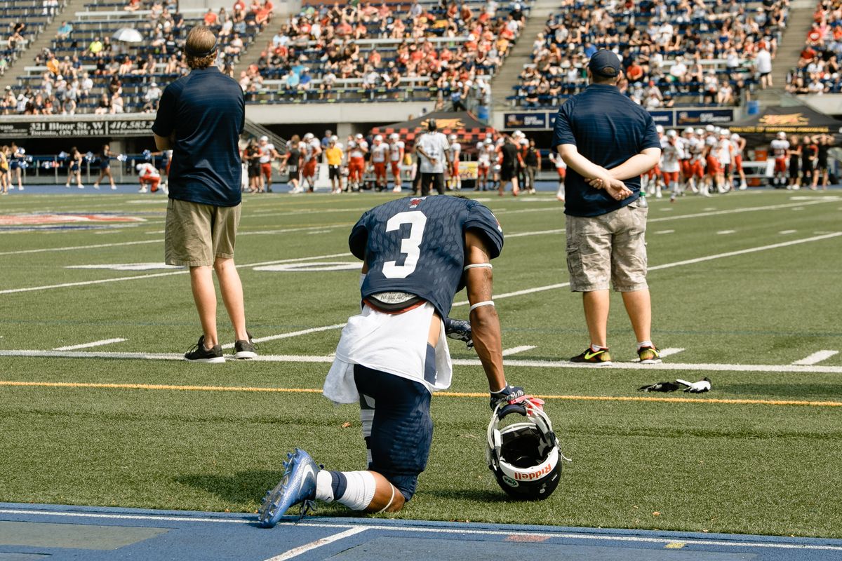 Rookie footballer kneeling on the field with his helmet