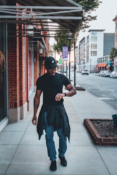 A stylish young man strolls downtown, checking his wristwatch while walking on the city sidewalk.
