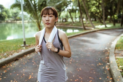 一名运动员脖子上围着毛巾，在公园里慢跑以增强健康