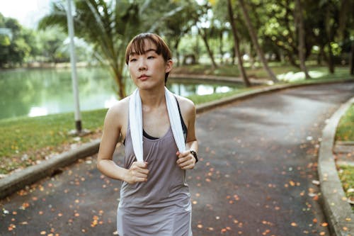 Serious ethnic female athlete wearing sportswear and smart watch looking away while jogging alone in park at daytime in summer day