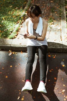 Ethnic woman sitting on border and browsing smartphone