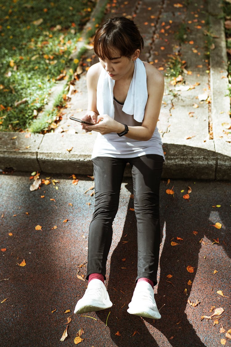 Ethnic Woman Sitting On Border And Browsing Smartphone