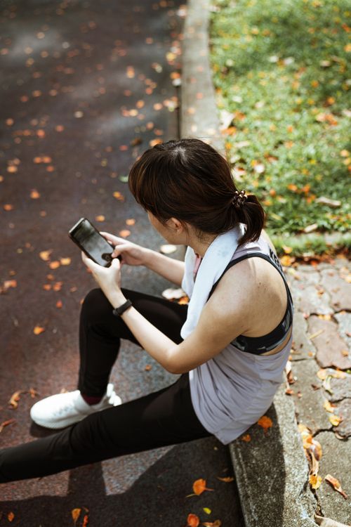 Free From above of female wearing sport clothes sitting on border and browsing smartphone while resting and searching information in internet Stock Photo