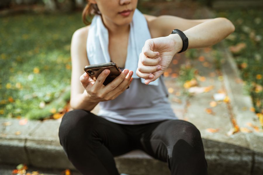 A person in sportswear checking a fitness smartwatch and holding a smartphone after a workout outdoors