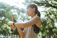 在阳光明媚的公园里，亚洲妇女正用智能手机查看健身追踪器