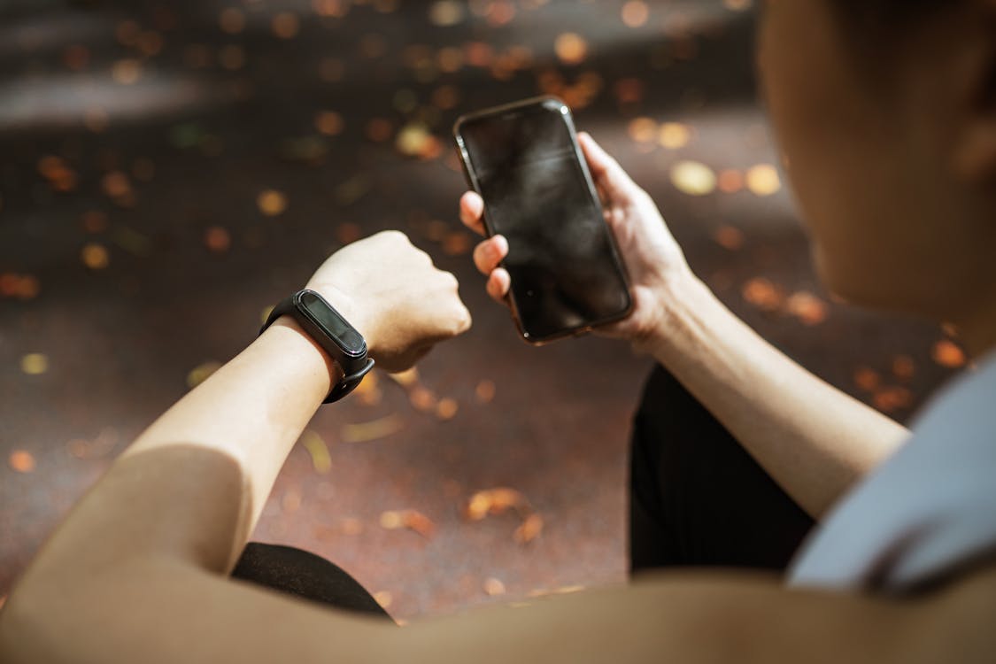 Free Back view of anonymous female using smartphone app and smart watch after jogging in park Stock Photo