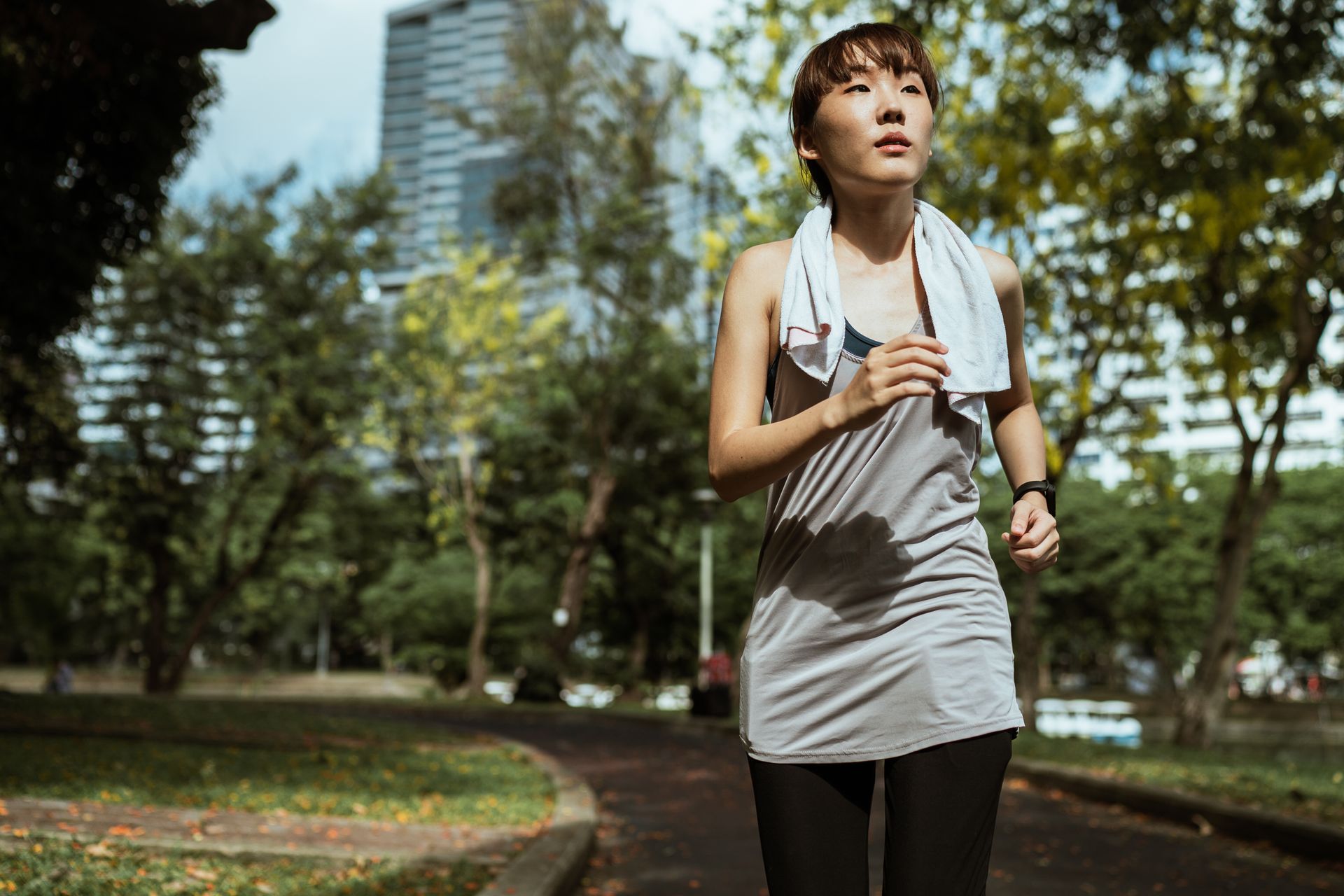 Sportive slim ethnic female in sportswear running on sidewalk in park in warm sunny day