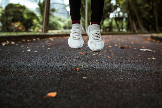 Feet of anonymous person in white sneakers jumping on sidewalk in park in summer morning