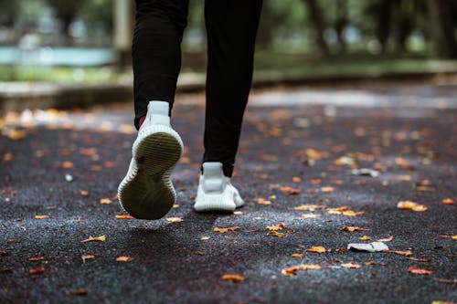 Legs of anonymous person in white sneakers and black leggings running on sidewalk