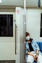 一名穿着牛仔夹克的亚洲女子戴着口罩躺在地铁座位上，这反映了疫情期间的生活方式