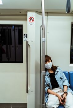 一名穿着牛仔夹克的亚洲女子戴着口罩躺在地铁座位上，这反映了疫情期间的生活方式