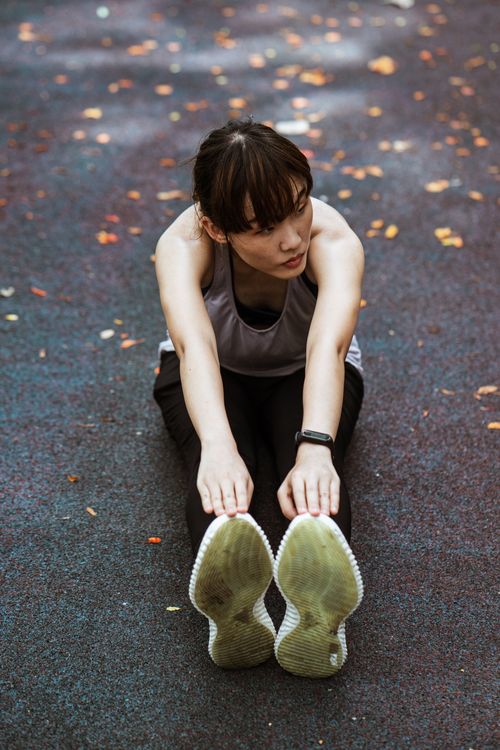 Free From above of flexible ethnic female in sportswear and sneakers sitting on pavement and bending forward while warming up and looking away Stock Photo
